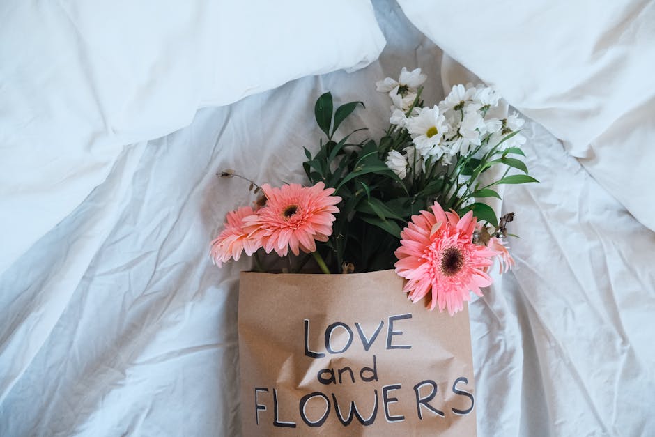 A floral arrangement featuring fresh pink gerbera daisies with large, vibrant petals and dark centers, alongside delicate white daisies with yellow centers, all arranged with green foliage. The flower
