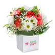 A touch of Barkingside's vibrant community is reflected in this joyful bouquet, nestled snugly within a pristine white square gift bag and poised to bring warmth to any occasion. The bouquet's coral and peach carnations, lush with ruffled petals, radiate a bright energy, softened by the airy presence of snow-white baby's breath and the playful pop of pure daisies with their green-gold eyes. The arrangement is accented with a handful of unopened, purple-tipped buds that lend a dash of intrigue, while the whole ensemble is wrapped in a cradle of polished green foliage, echoing the leafy settings of Barkingside's nearby parks. Designed in a perfectly balanced, rounded shape, this bouquet exudes freshness and celebration, ready for delivery to friends, neighbors, or loved ones along Fencepiece Road or at home after a stroll through Fullwell Cross. The elegant white ribbon handles hint at an easy gift-giving experience that will brighten birthdays, mark anniversaries, or simply say "thinking of you." Each flower is expertly chosen and artfully arranged, carrying with it the care and spirit that Barkingside florists are known for-making every delivery a gesture of happiness and heartfelt intent.